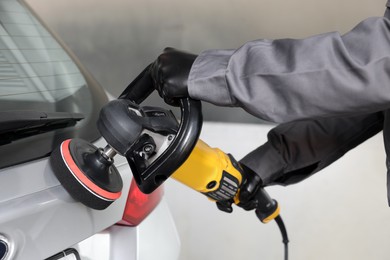 Photo of Man polishing car with orbital polisher indoors, closeup