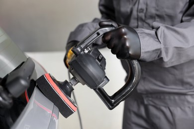 Photo of Man polishing car with orbital polisher indoors, closeup