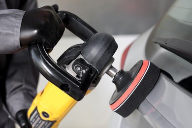 Photo of Man polishing car with orbital polisher indoors, closeup