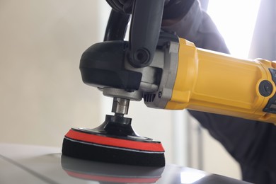 Photo of Man polishing car with orbital polisher indoors, closeup