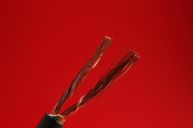 Photo of Stripped electrical wire with copper strands on red background, closeup