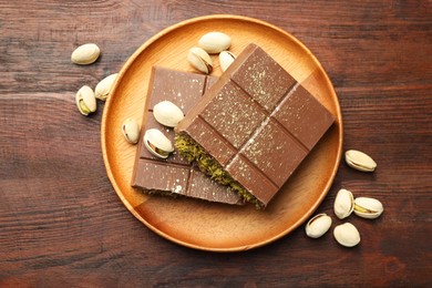 Photo of Pieces of tasty Dubai chocolate with pistachios and knafeh on wooden table, flat lay