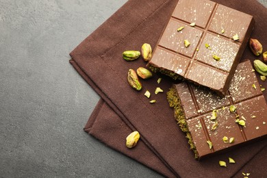 Photo of Pieces of tasty Dubai chocolate with pistachios and knafeh on grey table, top view. Space for text