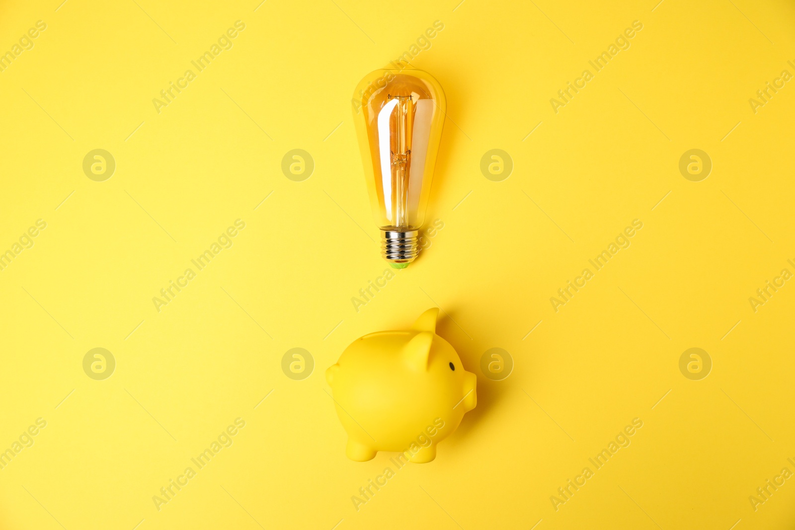 Photo of Light bulb and piggy bank on yellow background, flat lay. Energy saving concept