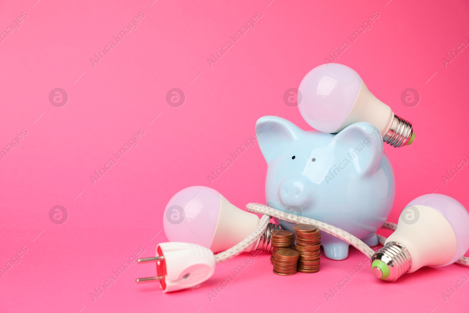 Photo of Piggy bank, light bulbs, coins and plug on pink background, space for text. Energy saving concept