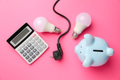 Photo of Piggy bank, calculator, light bulbs and plug on pink background, flat lay. Energy saving concept