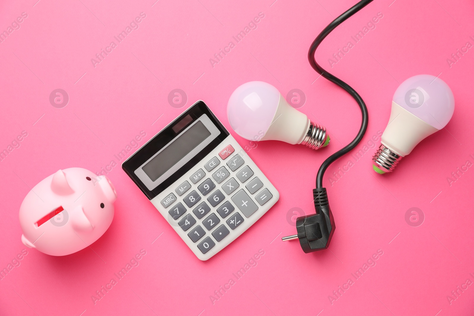 Photo of Piggy bank, calculator, light bulbs and plug on pink background, flat lay. Energy saving concept