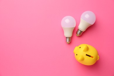 Photo of Piggy bank and light bulbs on pink background, flat lay with space for text. Energy saving concept