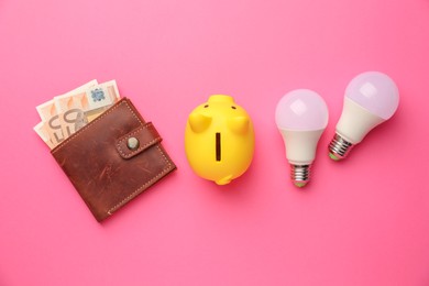 Photo of Piggy bank, light bulbs and purse with euro banknotes on pink background, flat lay. Energy saving concept