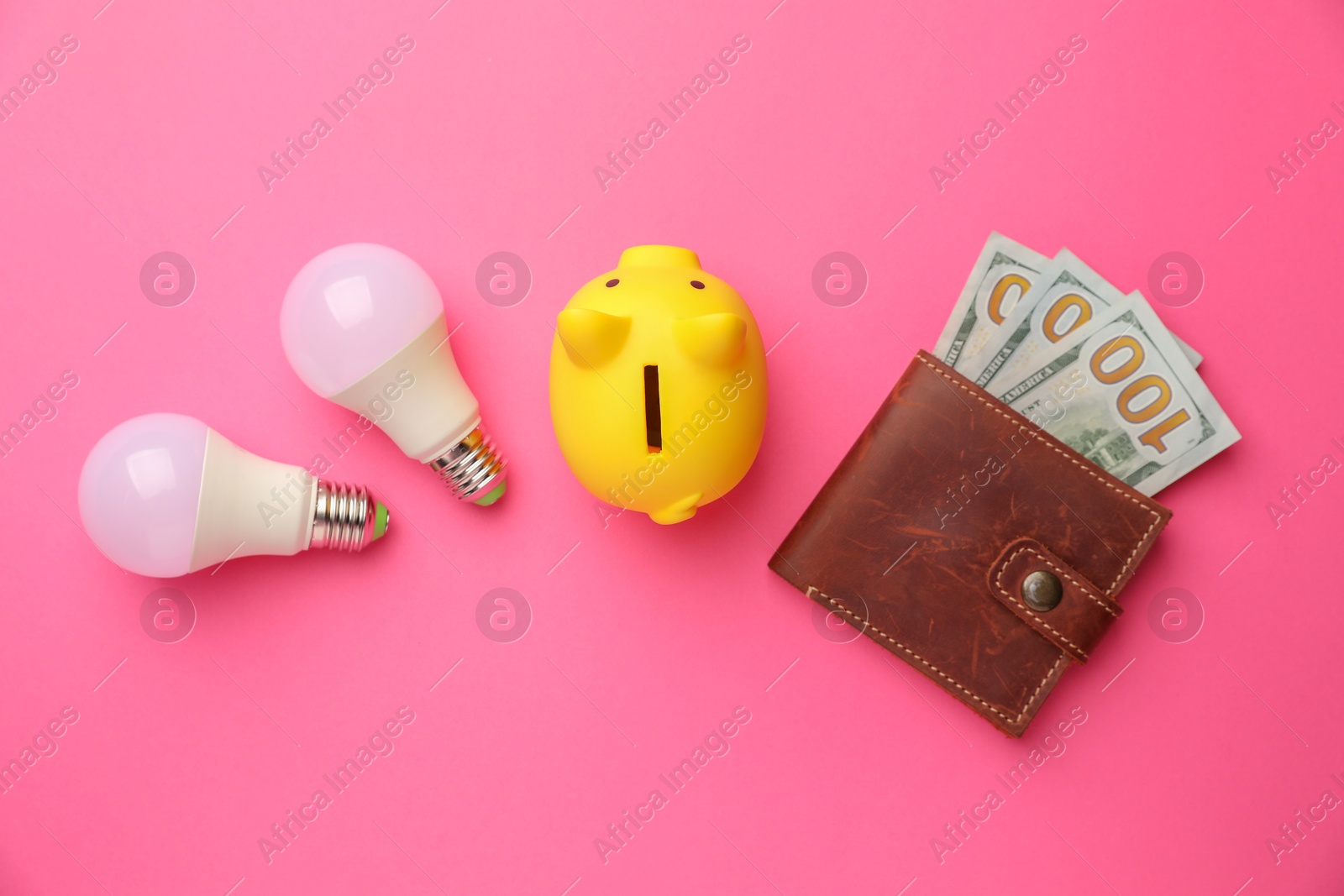 Photo of Piggy bank, light bulbs and purse with dollar banknotes on pink background, flat lay. Energy saving concept