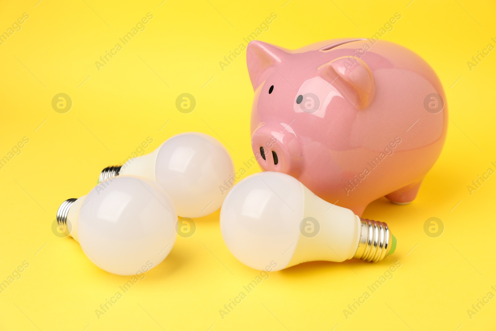 Photo of Piggy bank and light bulbs on yellow background, closeup. Energy saving concept