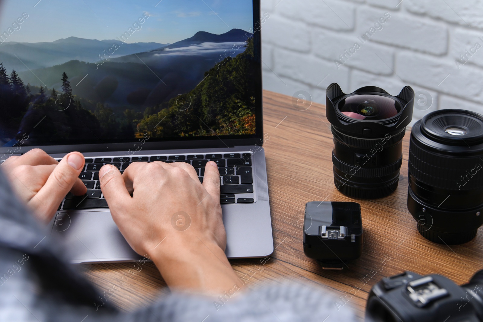 Photo of Photographer with laptop and lens at wooden table, closeup