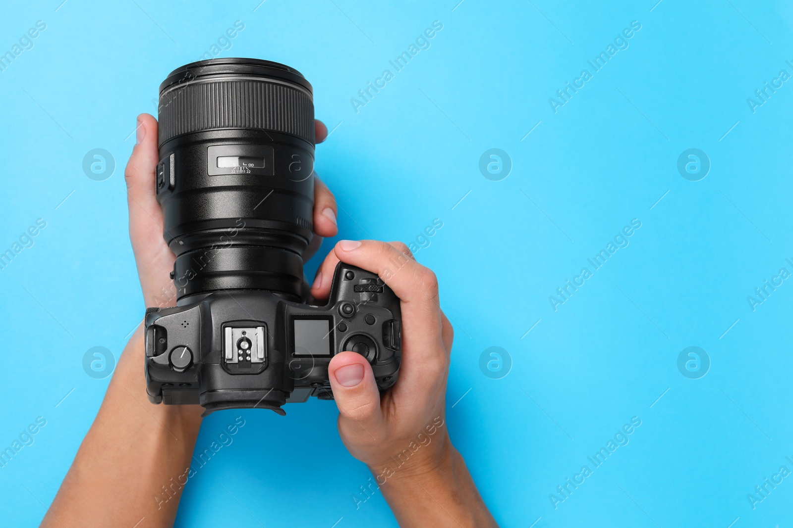 Photo of Photographer with professional camera on light blue background, top view. Space for text