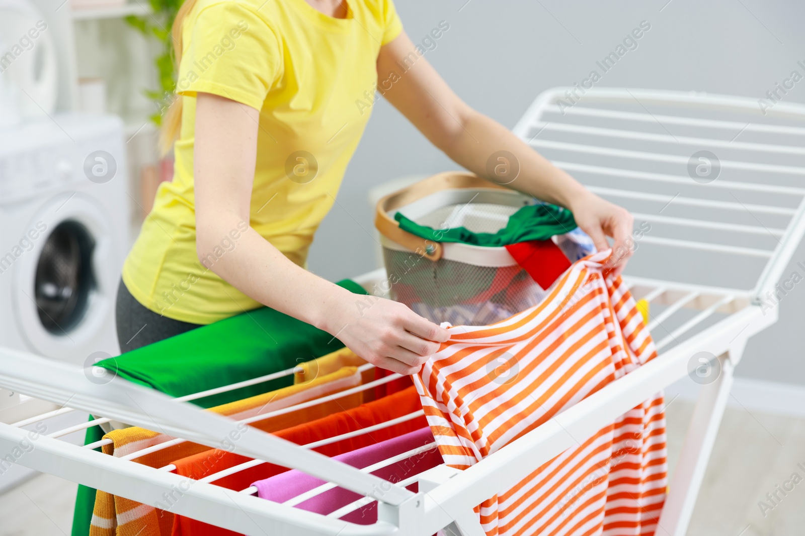 Photo of Woman hanging fresh clean laundry on drying rack at home, closeup