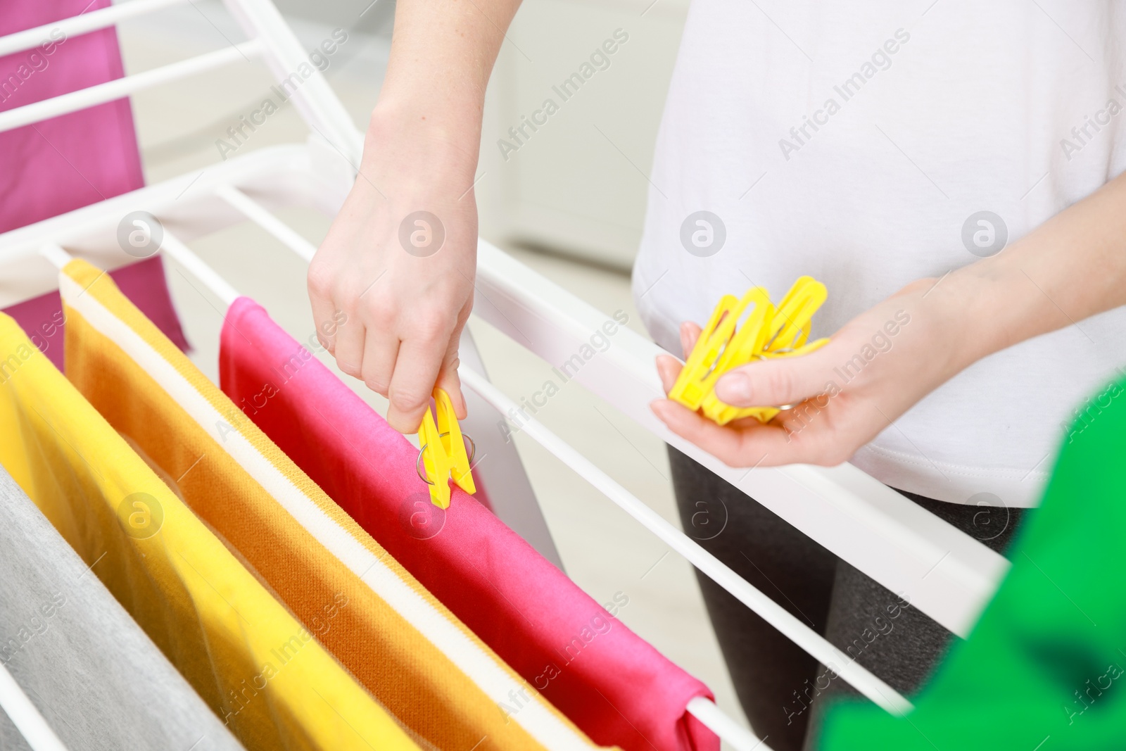 Photo of Woman hanging fresh clean laundry on drying rack at home, closeup