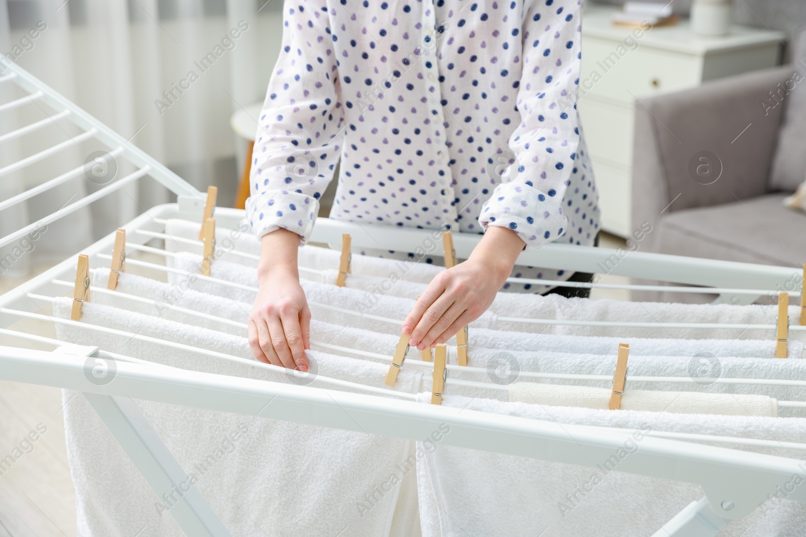 Photo of Woman hanging fresh clean laundry on drying rack at home, closeup