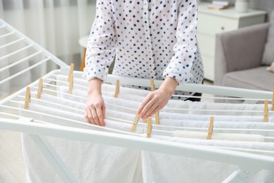 Photo of Woman hanging fresh clean laundry on drying rack at home, closeup