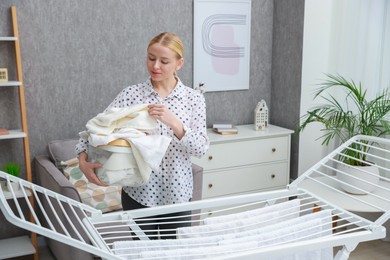 Photo of Beautiful woman hanging fresh clean laundry on drying rack at home