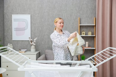 Beautiful woman hanging fresh clean laundry on drying rack at home