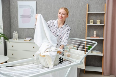 Photo of Beautiful woman hanging fresh clean laundry on drying rack at home