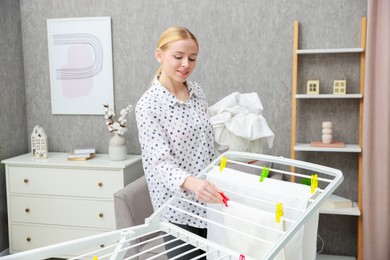 Photo of Beautiful woman hanging fresh clean laundry on drying rack at home