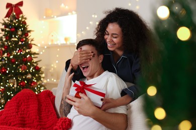 Happy girlfriend surprising her boyfriend with Christmas gift at home