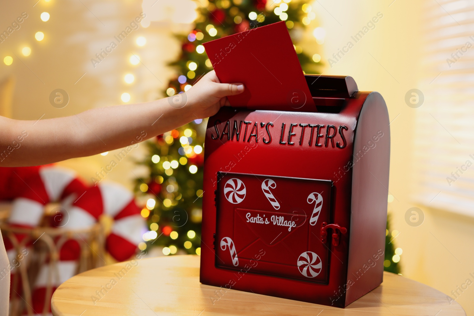 Photo of Little child putting letter to Santa Claus into red mail box indoors, closeup. Christmas tradition