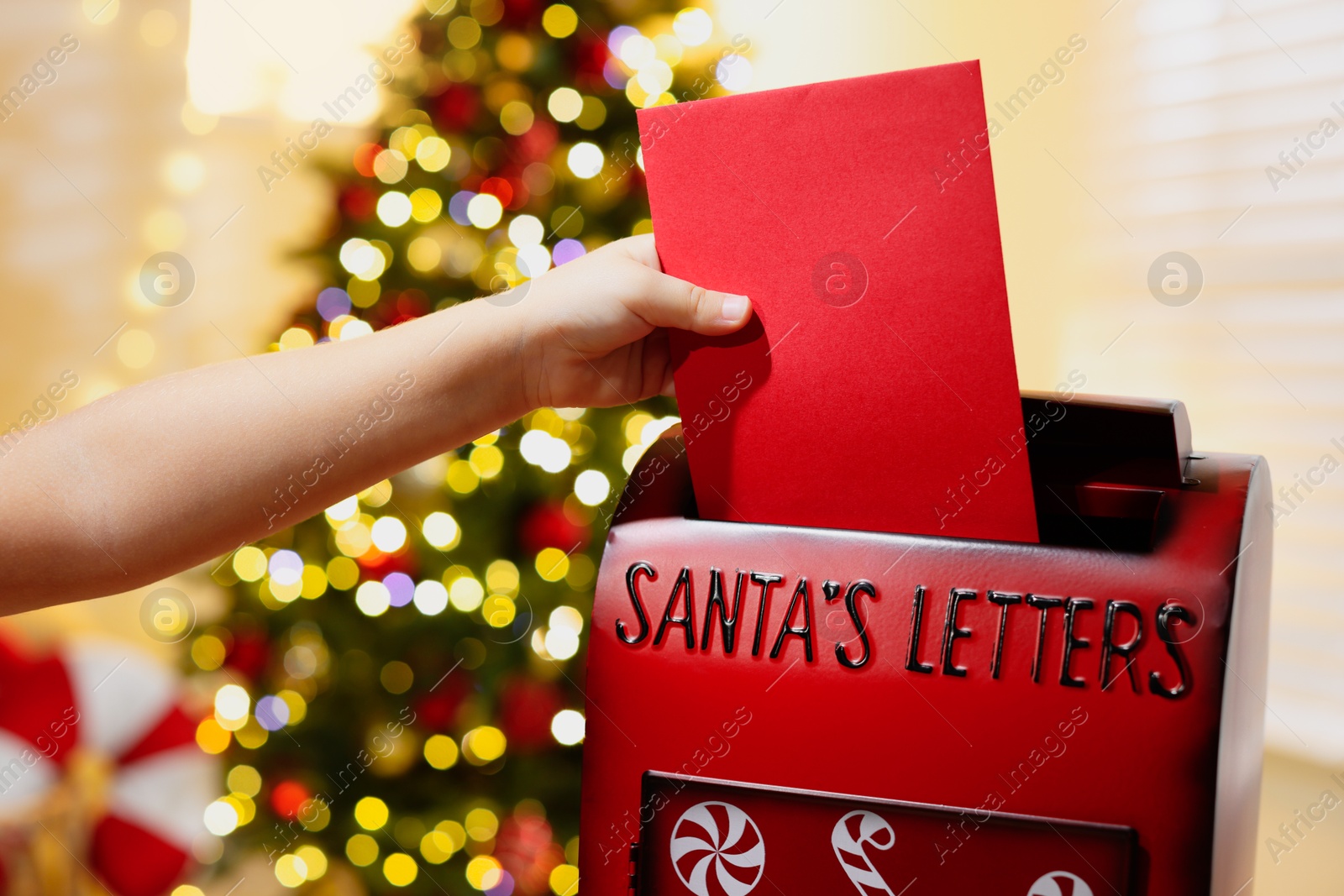 Photo of Little child putting letter to Santa Claus into red mail box indoors, closeup. Christmas tradition