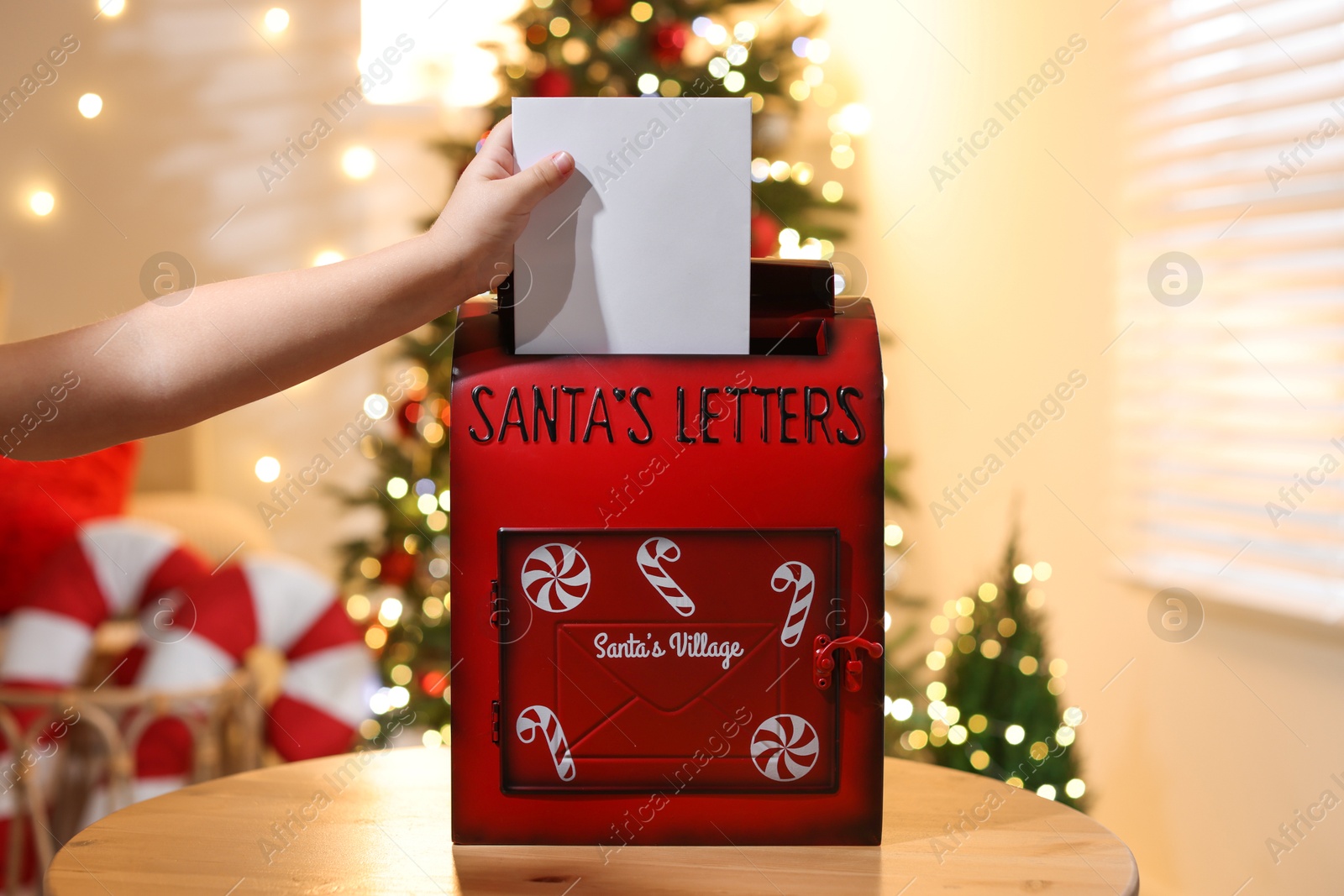 Photo of Little child putting letter to Santa Claus into red mail box indoors, closeup. Christmas tradition