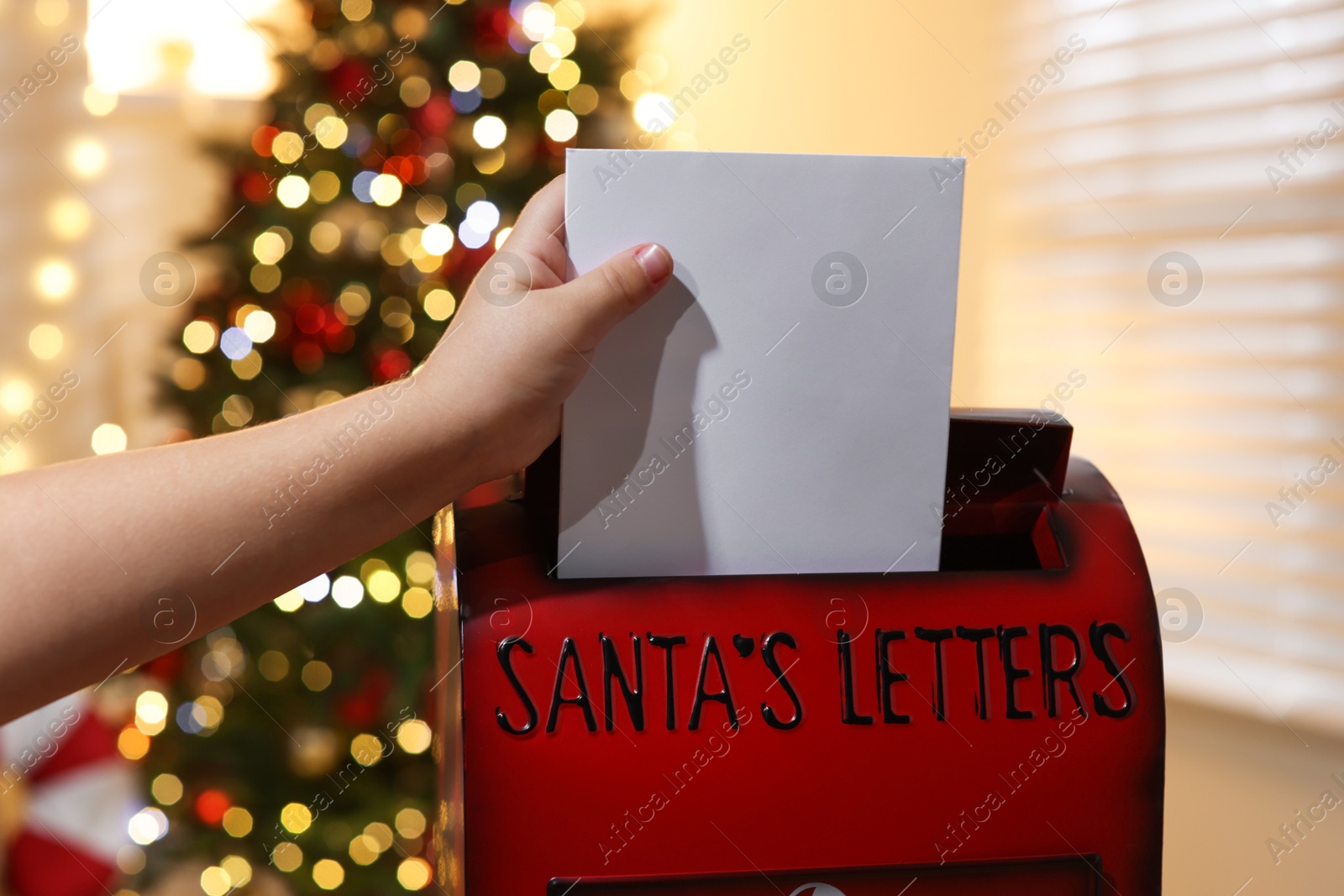 Photo of Little child putting letter to Santa Claus into red mail box indoors, closeup. Christmas tradition