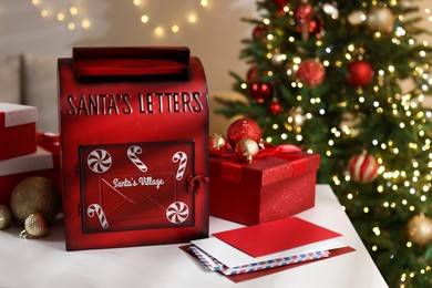 Photo of Santa Claus mailbox, letters, gift boxes and festive decor on white table indoors. Christmas atmosphere