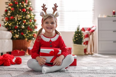 Photo of Little girl in Christmas costume with gift boxes at home