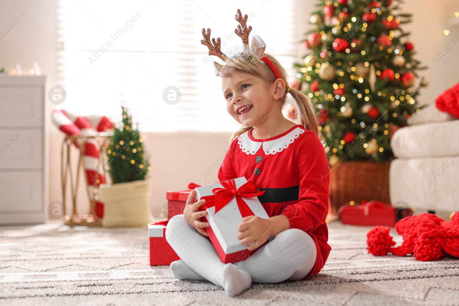 Photo of Little girl in Christmas costume with gift boxes at home