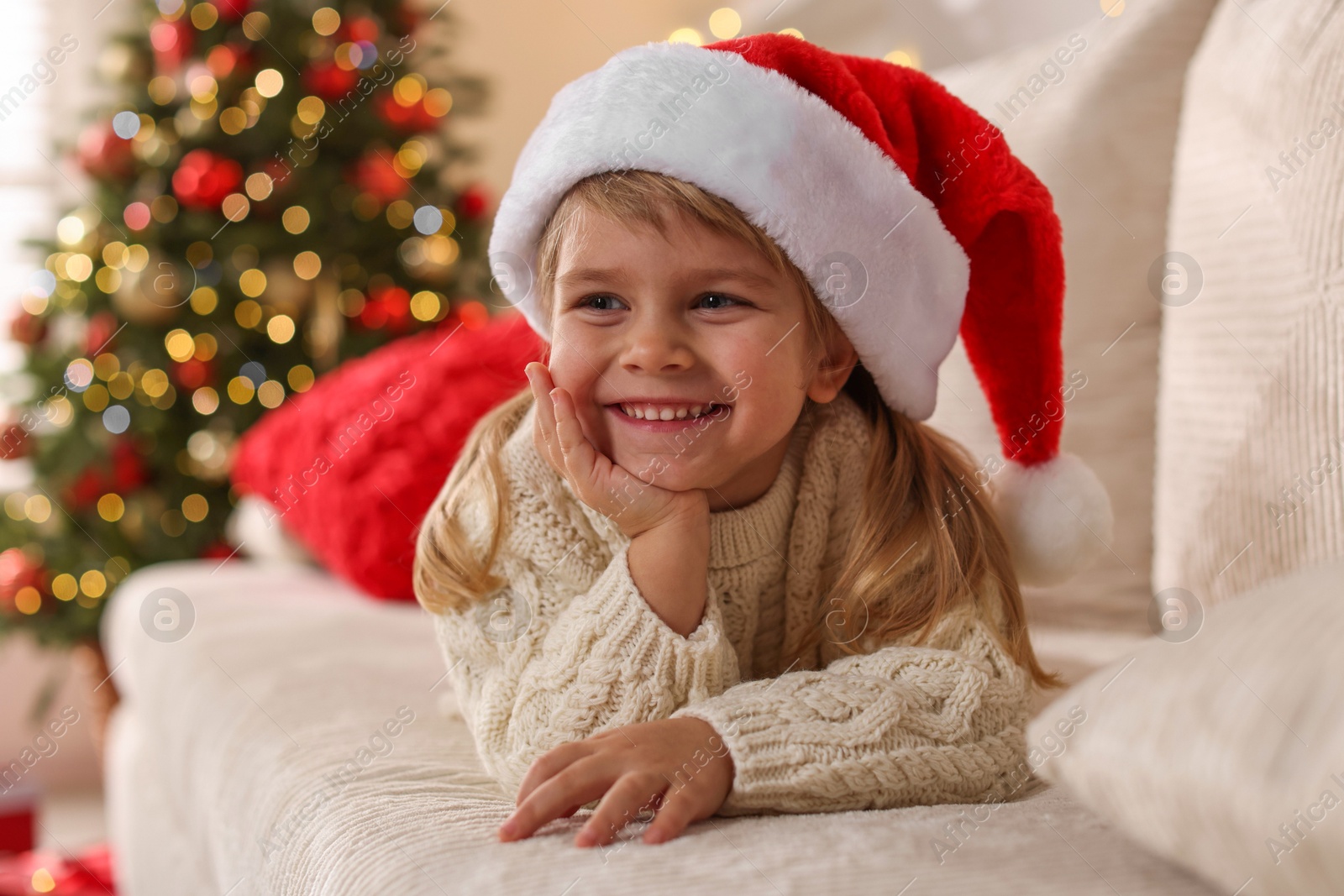 Photo of Little girl in Santa hat lying on sofa at home