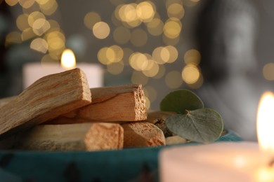 Photo of Palo santo sticks, eucalyptus leaves and burning candles on table, closeup