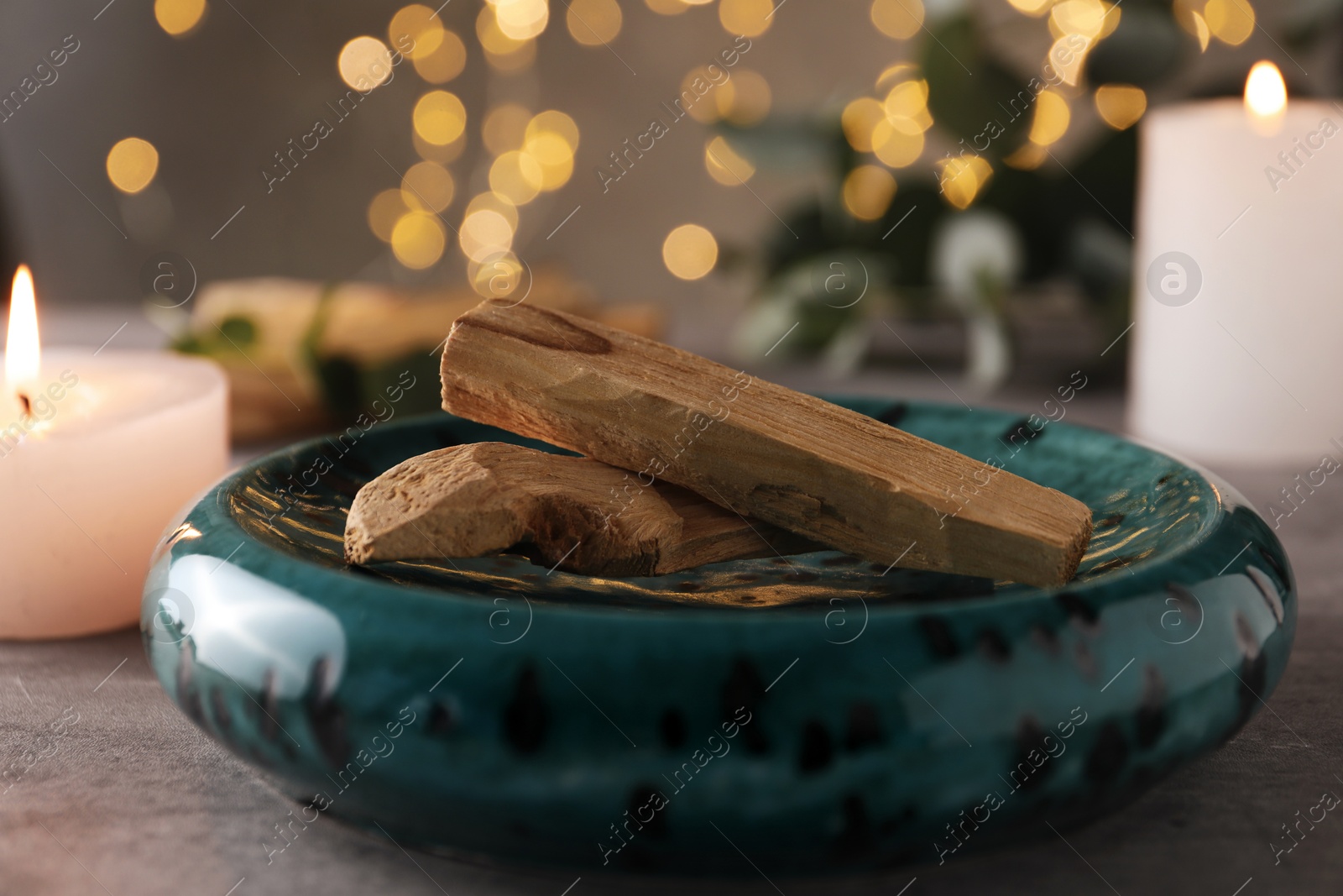 Photo of Palo santo sticks and burning candles on grey table, closeup