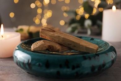 Photo of Palo santo sticks and burning candles on grey table, closeup