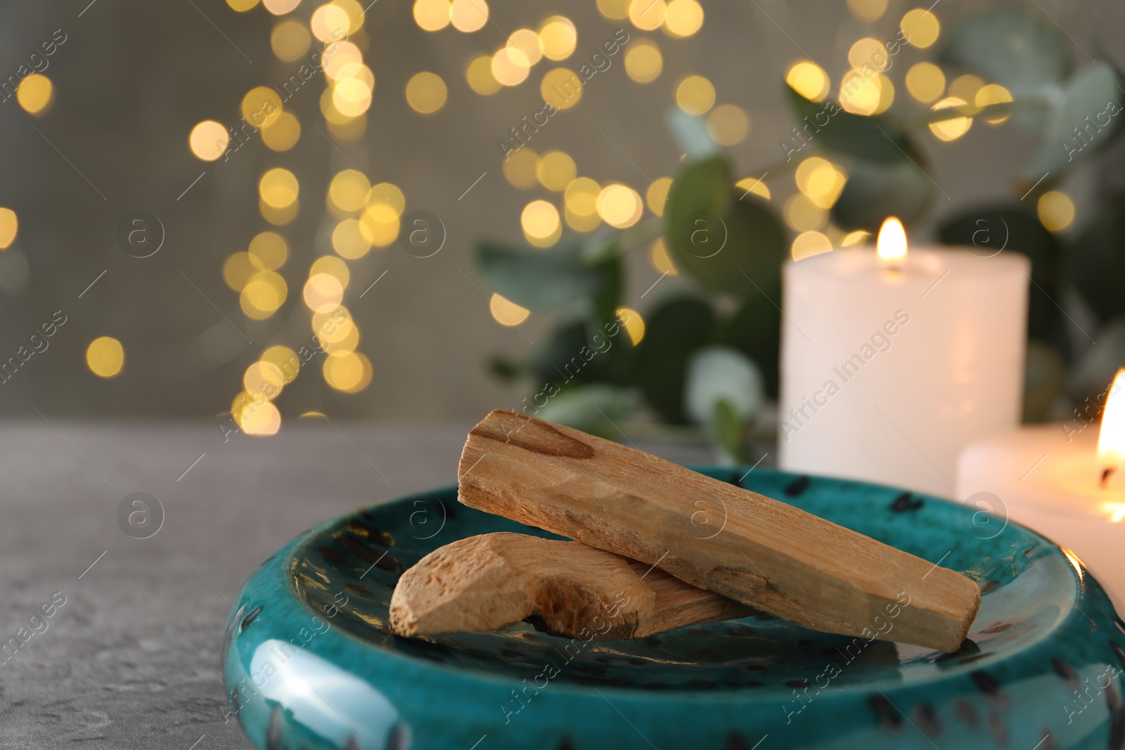 Photo of Palo santo sticks and burning candles on grey table, closeup