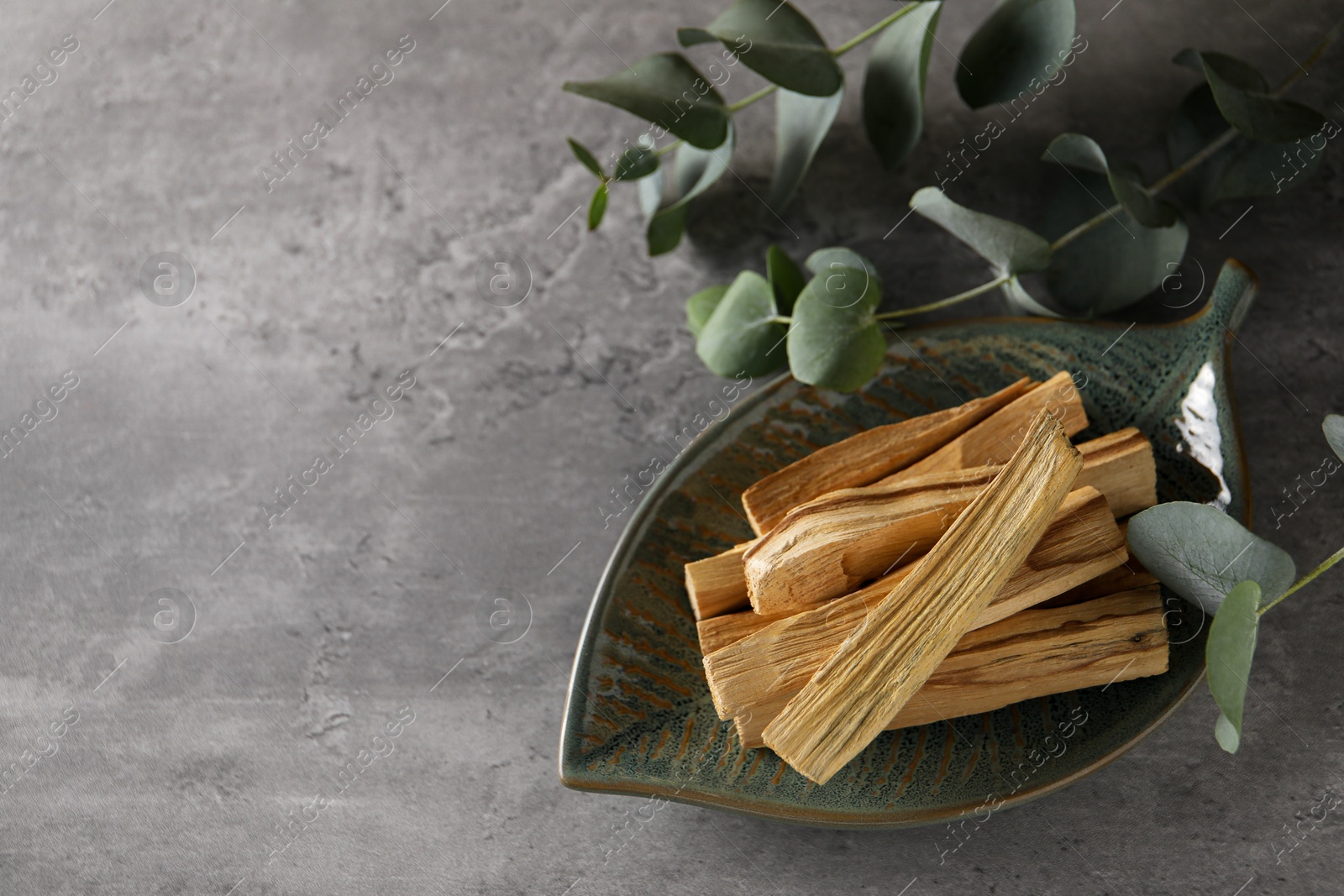 Photo of Palo santo sticks and eucalyptus leaves on grey table, closeup. Space for text