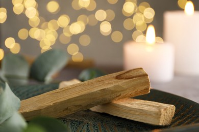 Photo of Palo santo sticks, eucalyptus leaves and burning candles on table, closeup