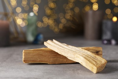 Photo of Palo santo sticks on grey table against blurred lights, closeup