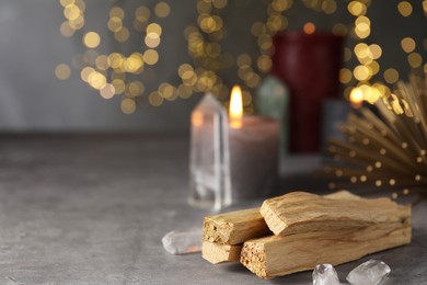 Photo of Palo santo sticks and gemstones on grey table against blurred lights. Space for text