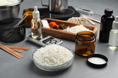 Photo of Soy wax, essential oil and different tools for making candles on gray textured table, closeup