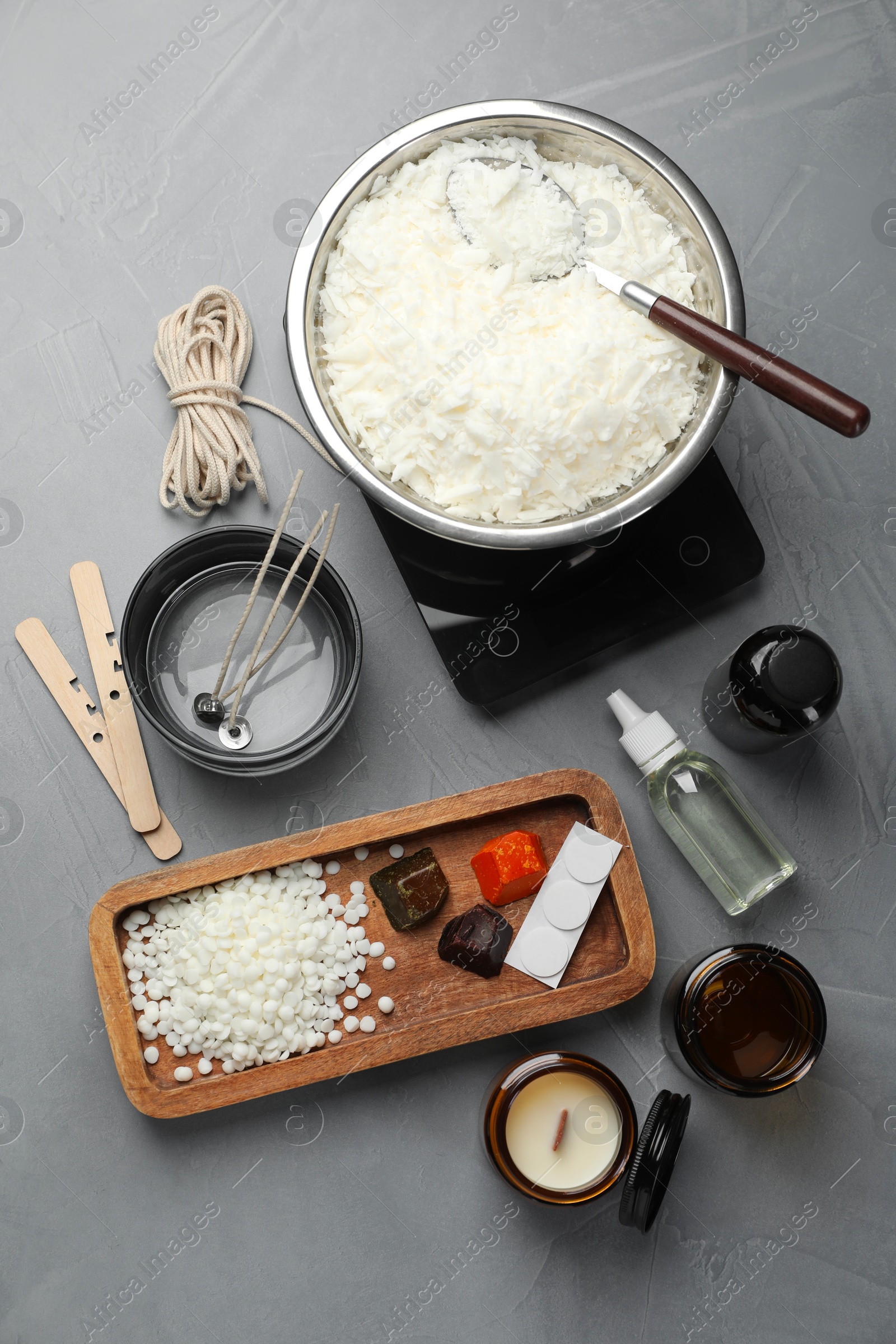 Photo of Soy wax, essential oils and different tools for making candles on gray textured table, flat lay