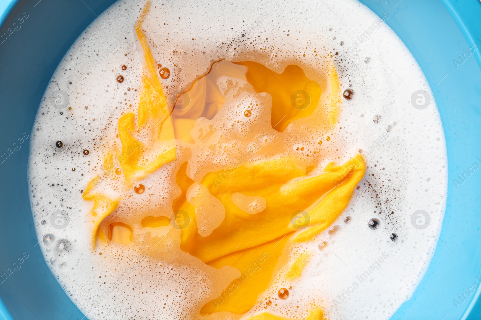 Photo of Yellow clothes soaked in water before washing, top view