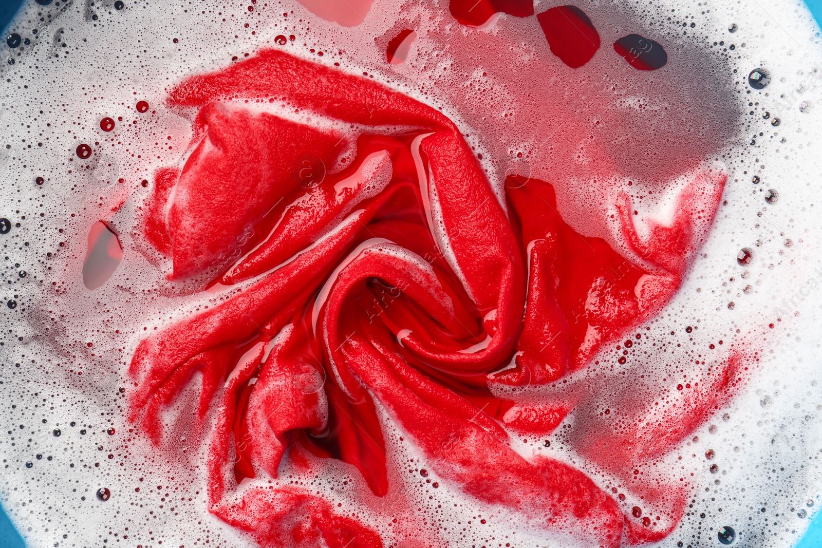 Photo of Red clothes soaked in water before washing, top view