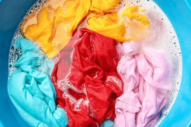 Photo of Colorful clothes soaked in water before washing, top view