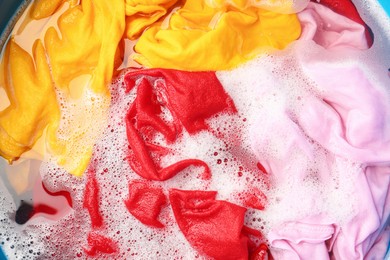 Photo of Colorful clothes soaked in water before washing, top view