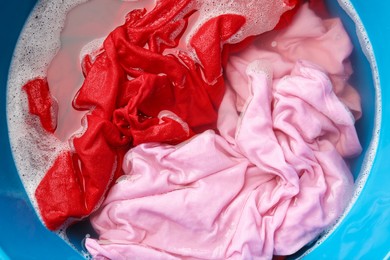 Photo of Colorful clothes soaked in water before washing, top view