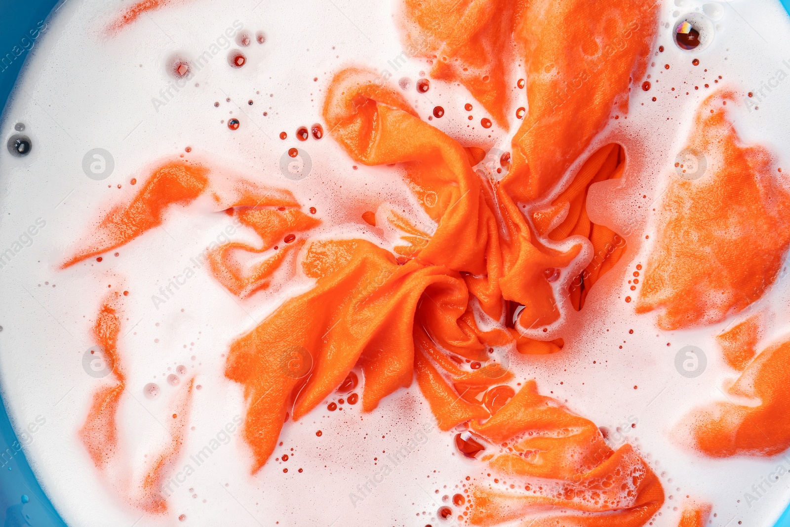 Photo of Orange clothes soaked in water before washing, top view